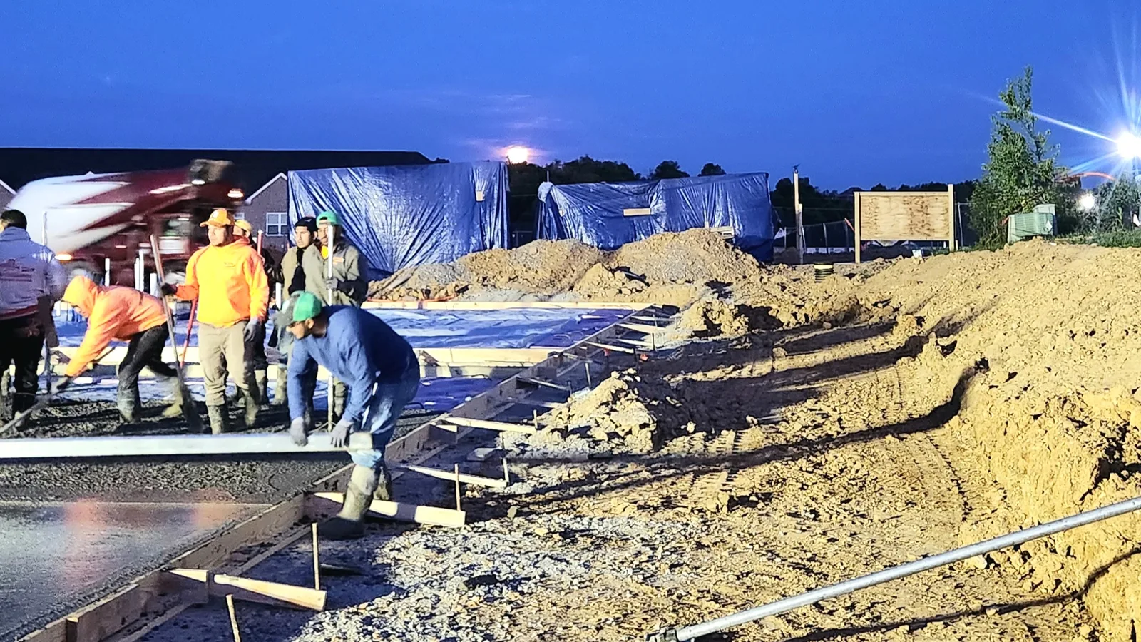 Crew screeding a fresh slab at dusk on a commercial job site, concrete contractor