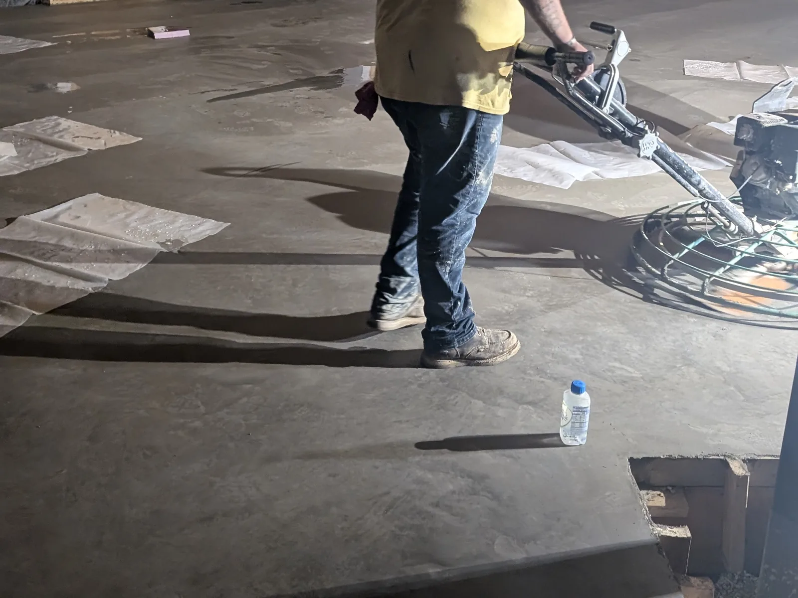 Worker running a floor machine over an interior slab in a building under construction, commercial concrete