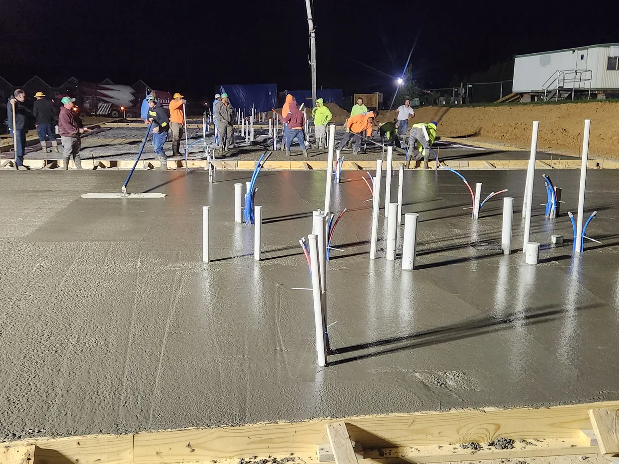 Crew placing a large slab at night under work lights with rebar dowels standing up, commercial concrete