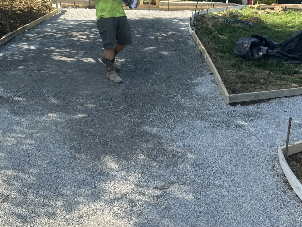 Compacted gravel base inside wood forms for a new driveway with a crew member walking across it, concrete driveways