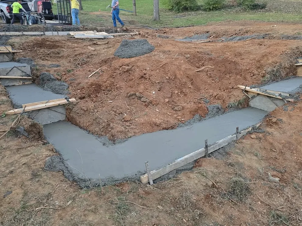 Freshly poured concrete footings in an excavated site with the crew behind, concrete foundations
