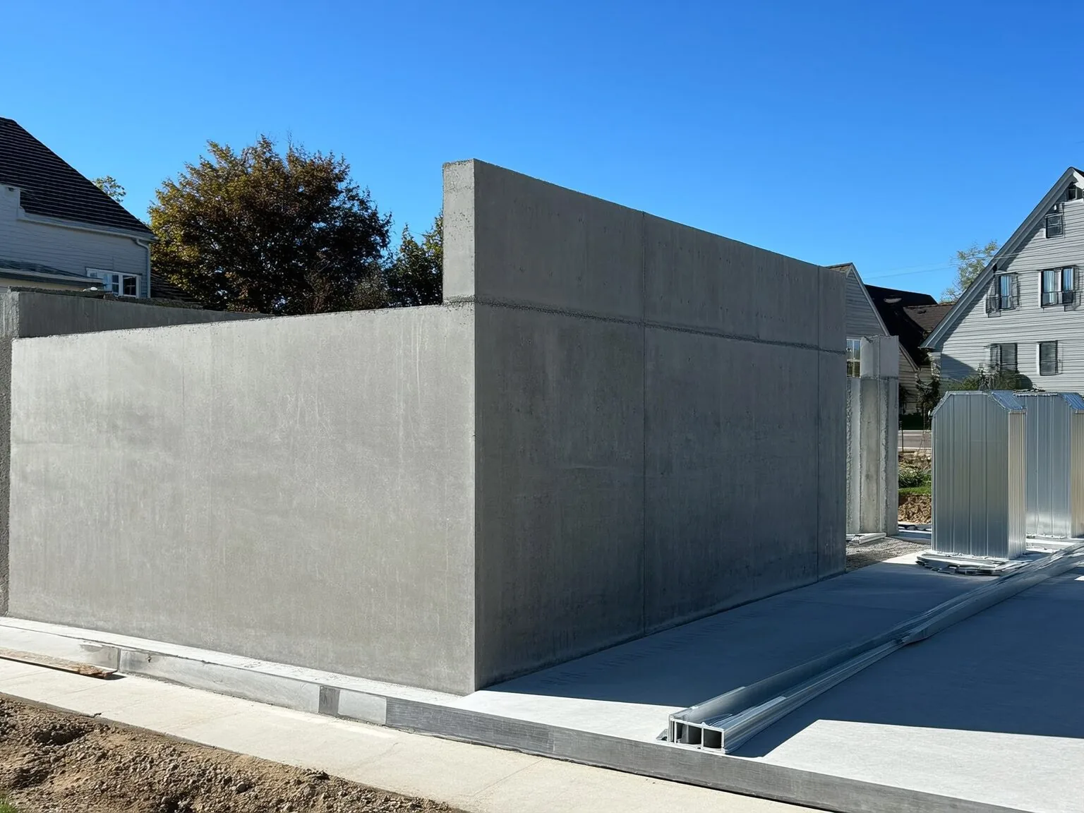 Poured concrete foundation wall on its footing beside a slab with form panels standing by, concrete foundations