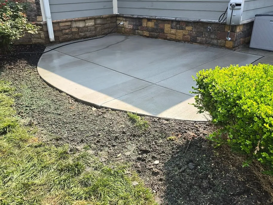 Curved concrete patio beside a house with a stone veneer base, concrete patios