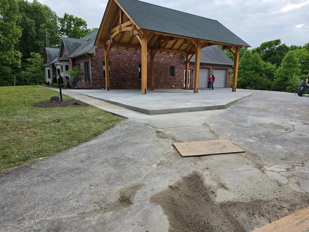 Finished concrete slab under a timber pavilion beside a brick house, concrete patios