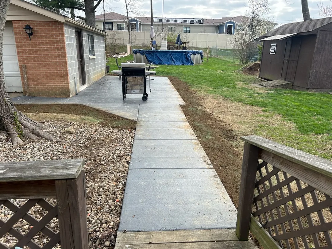 Long concrete walkway across a backyard beside a lattice fence, concrete sidewalks