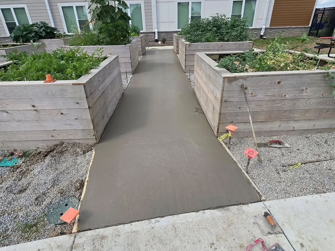 Fresh concrete walkway between raised garden beds outside an apartment building, concrete sidewalks