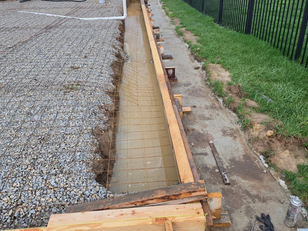 Slab forms with wire mesh over a gravel base beside a black fence, concrete slabs
