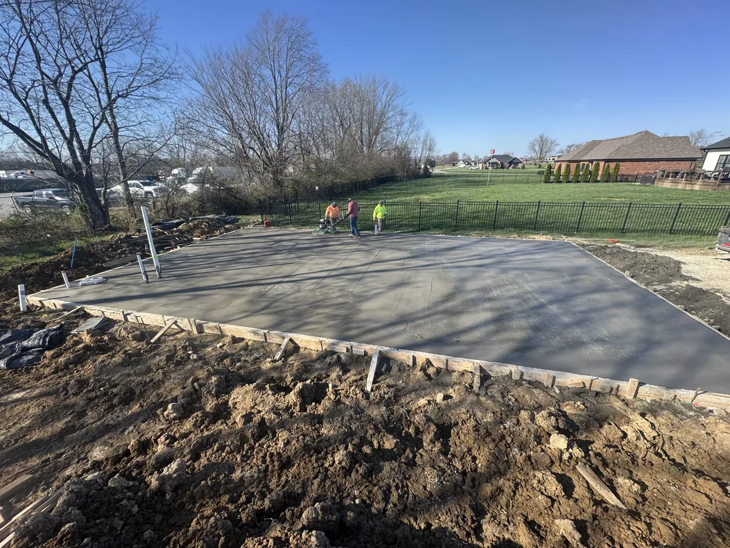 Crew placing a large concrete slab on an open lot with homes behind, concrete slabs