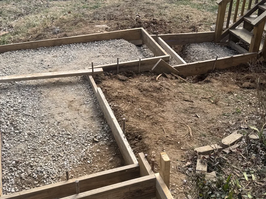 Wood forms set for concrete steps on a gravel base beside a deck, concrete steps