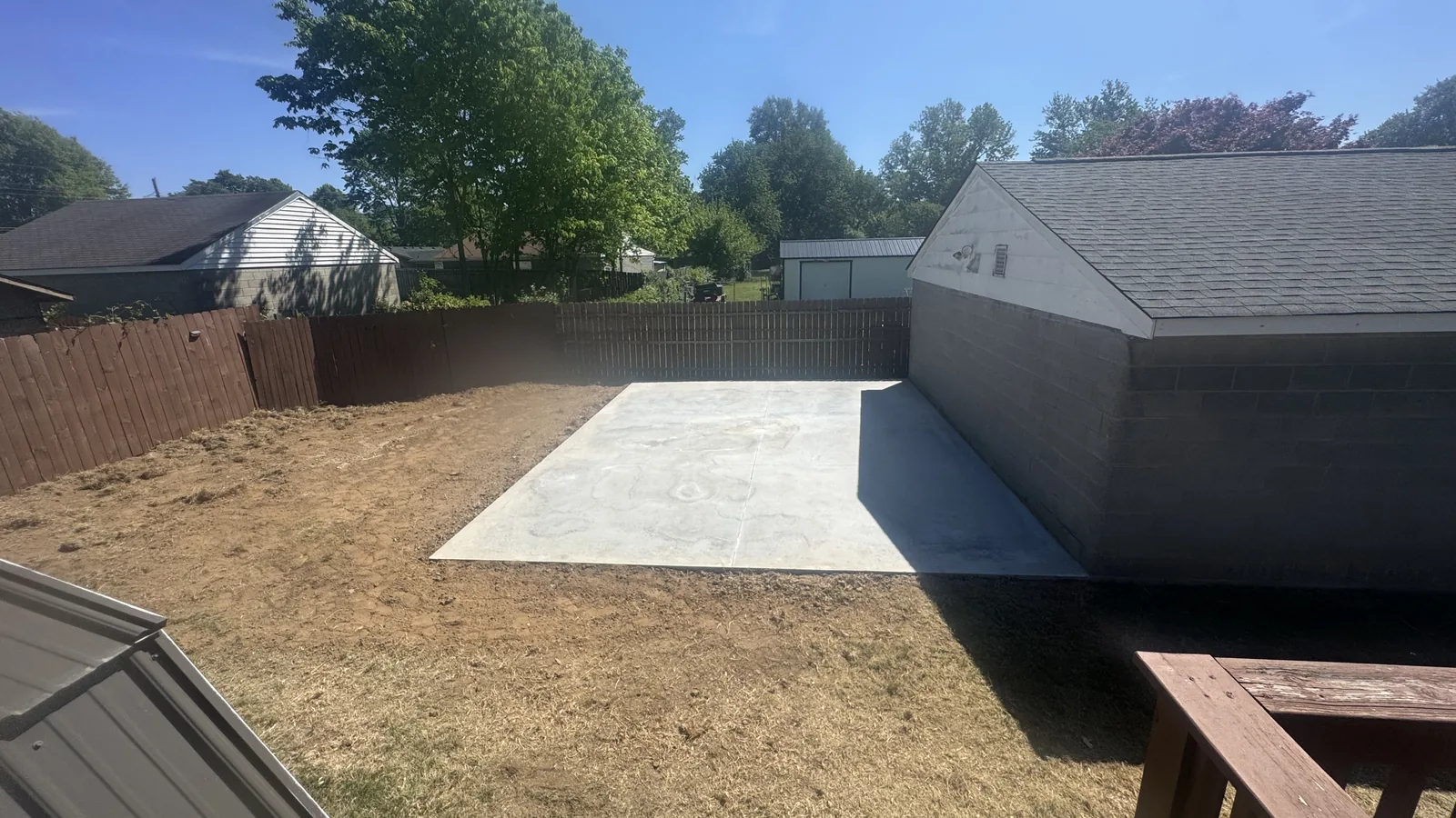New concrete pad in a fenced backyard beside a garage, concrete contractor