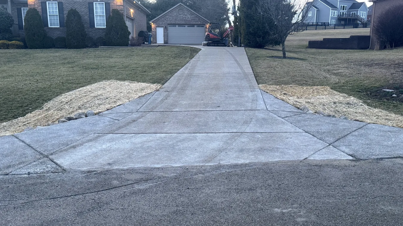 New concrete driveway with control joints running from the street up to a brick garage, concrete contractor