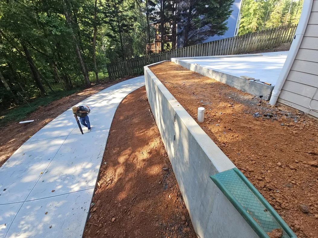 Poured concrete retaining wall holding a pad above a curved walkway on a sloped lot, concrete retaining walls
