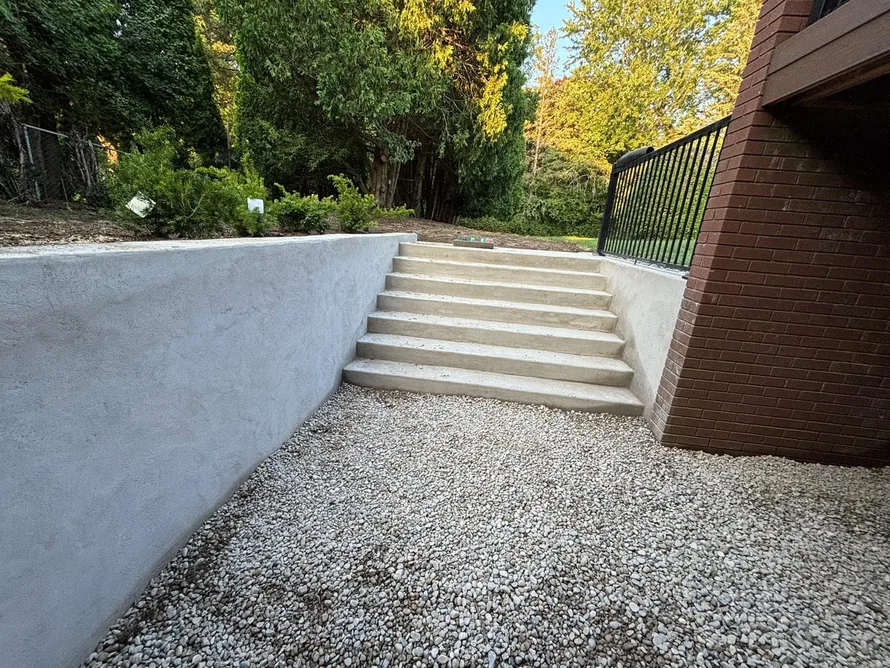Poured concrete retaining walls and steps beside a brick house above a gravel area, concrete retaining walls