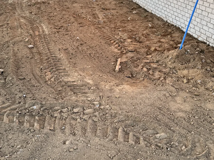 Graded dirt with machine tracks beside a brick house, site grading