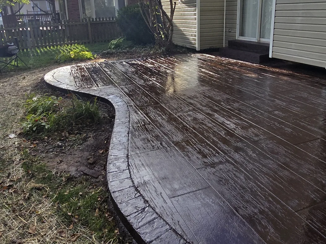 Dark colored stamped concrete patio with a curved border beside a house, stamped concrete