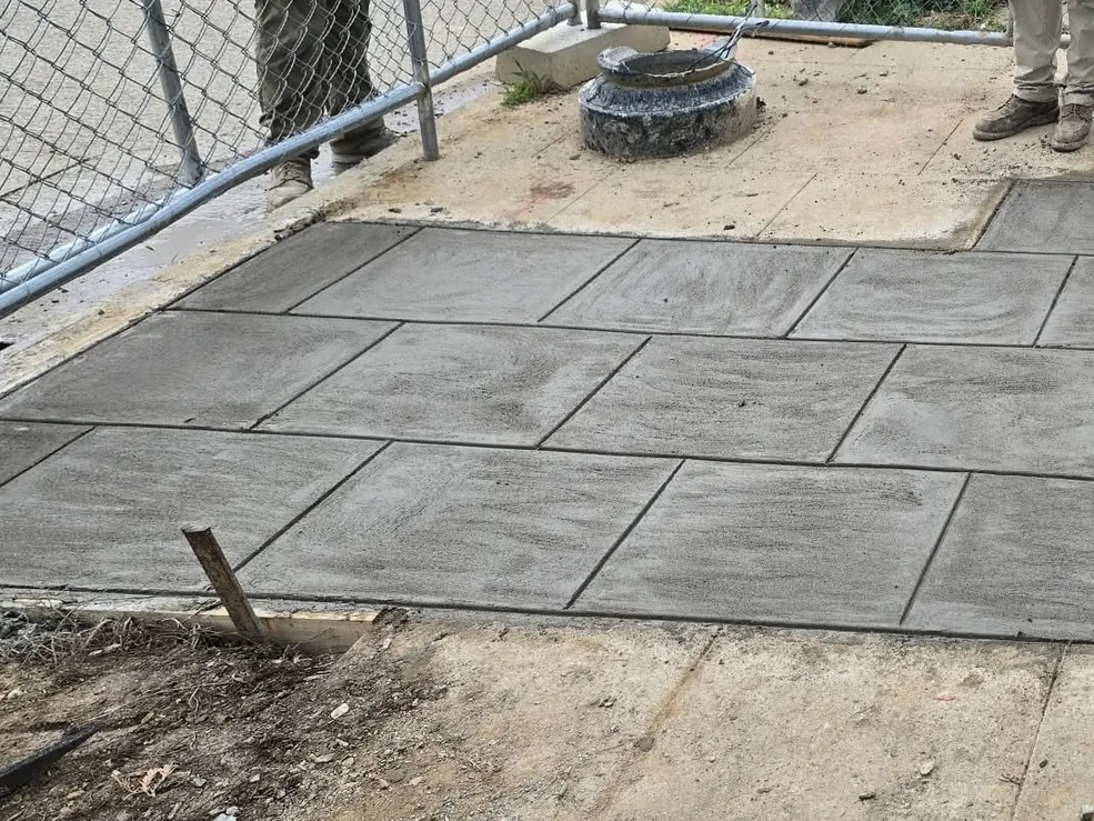 Stamped concrete patio in a slate pattern beside a chain link fence, stamped concrete